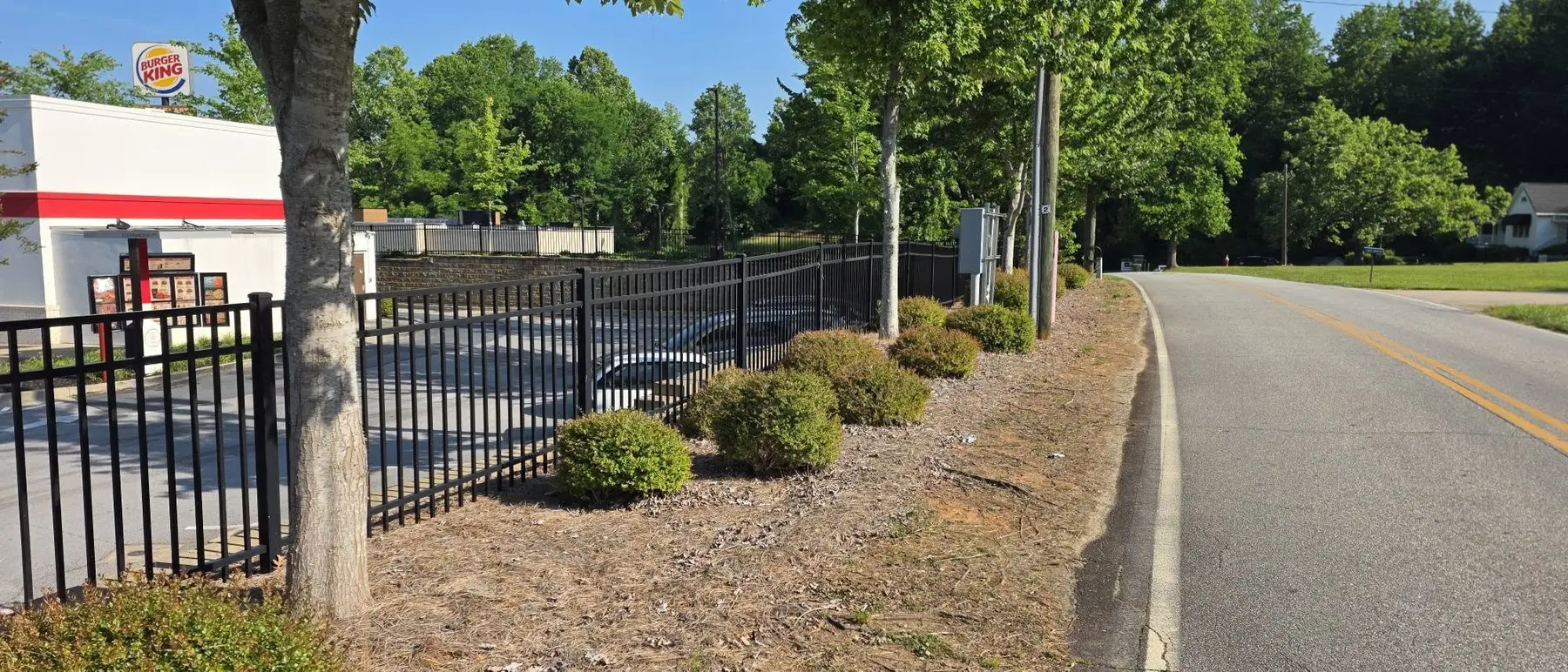 Overgrown fence-line landscaping before trimming and bed cleanup