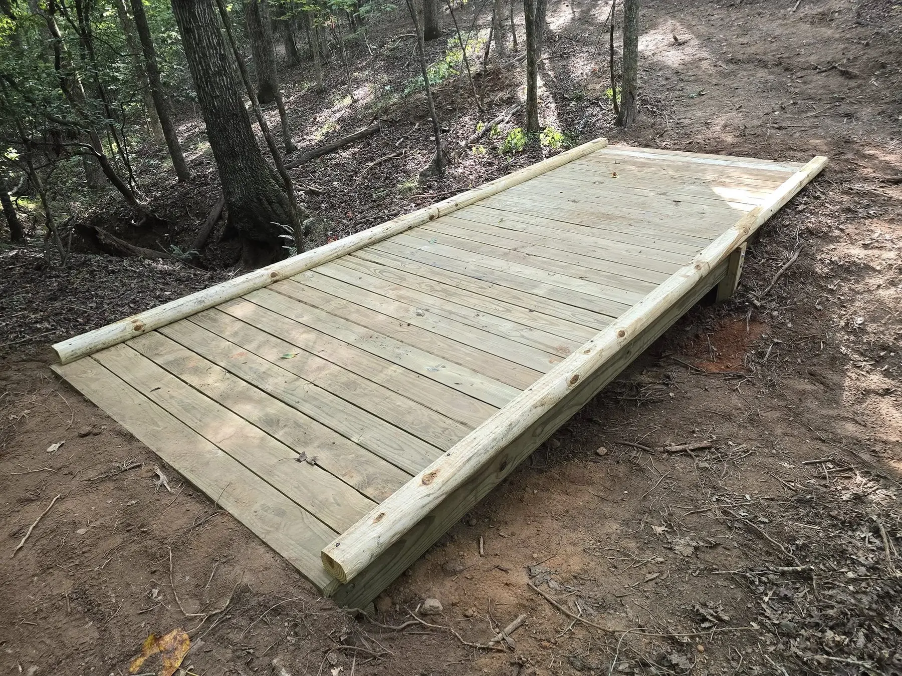 Custom pressure-treated wood bridge crossing a wooded property trail